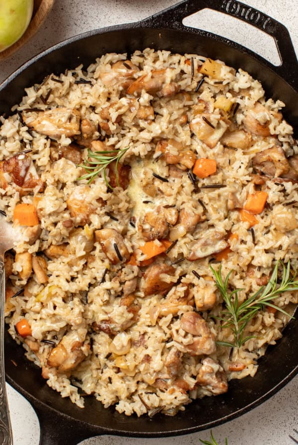 A chicken and wild rice skillet with fresh herbs and vegetables on a white table.