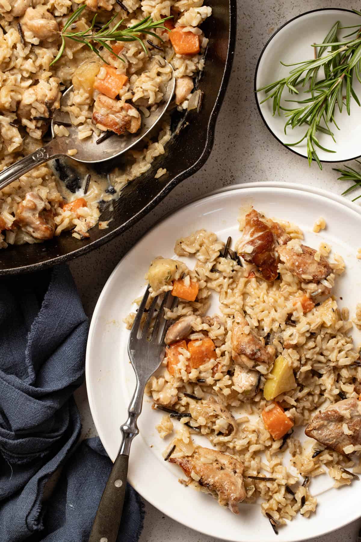 Chicken and rice scooped onto a white plate next to fresh rosemary sprigs and a glass of water.