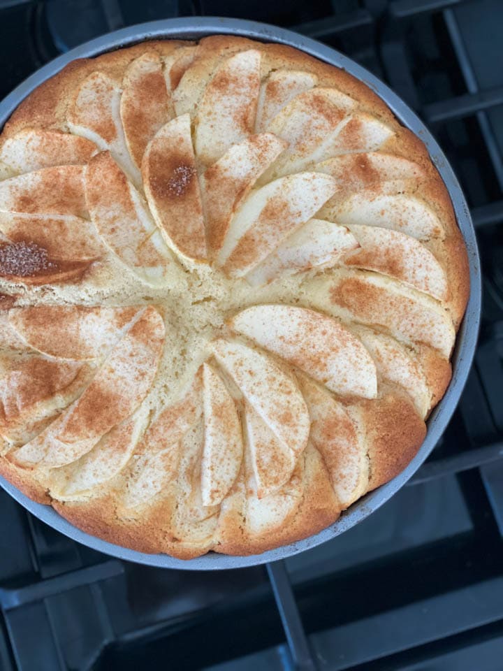 An apple cake in a cake pan coming out of the oven