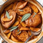 Apple cider pork chops in a cast iron pan with sage leaves on top.