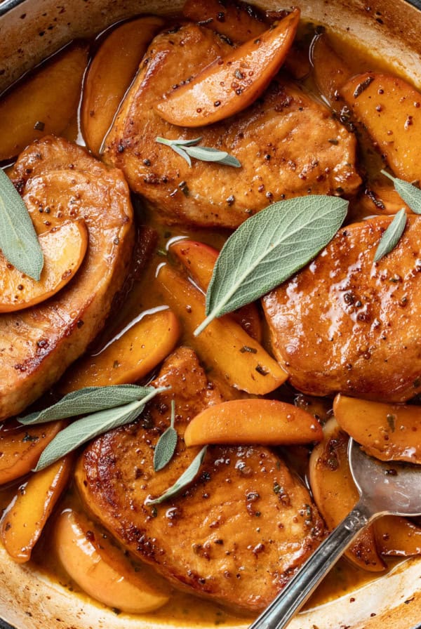 Apple cider pork chops in a cast iron pan with sage leaves on top.