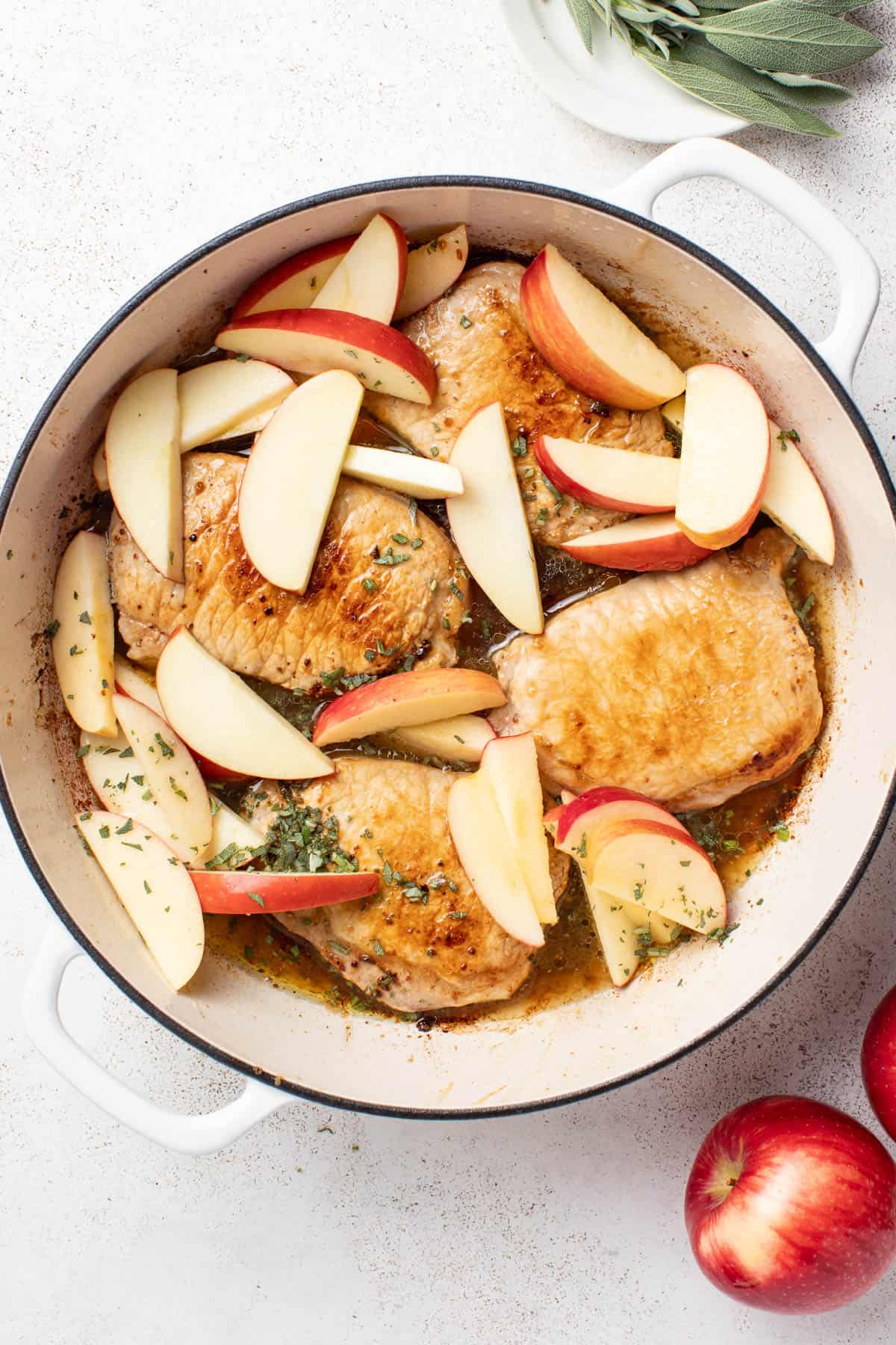 Adding apples to the pan with the pork chops.