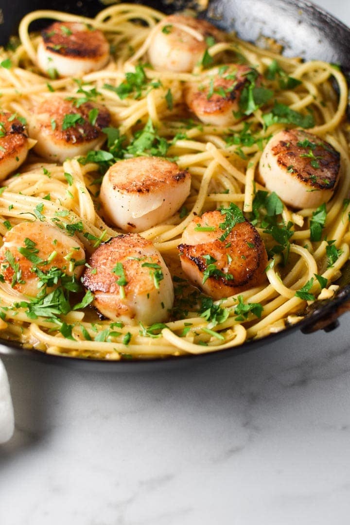A close up image of seared scallops on top of linguine pasta