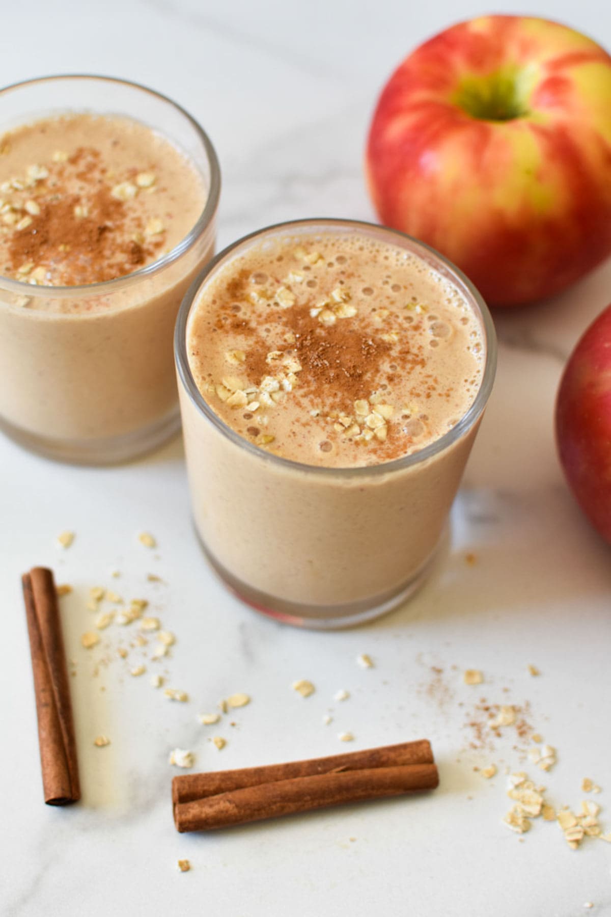 Two apple oatmeal smoothies with cinnamon sticks and oats. 