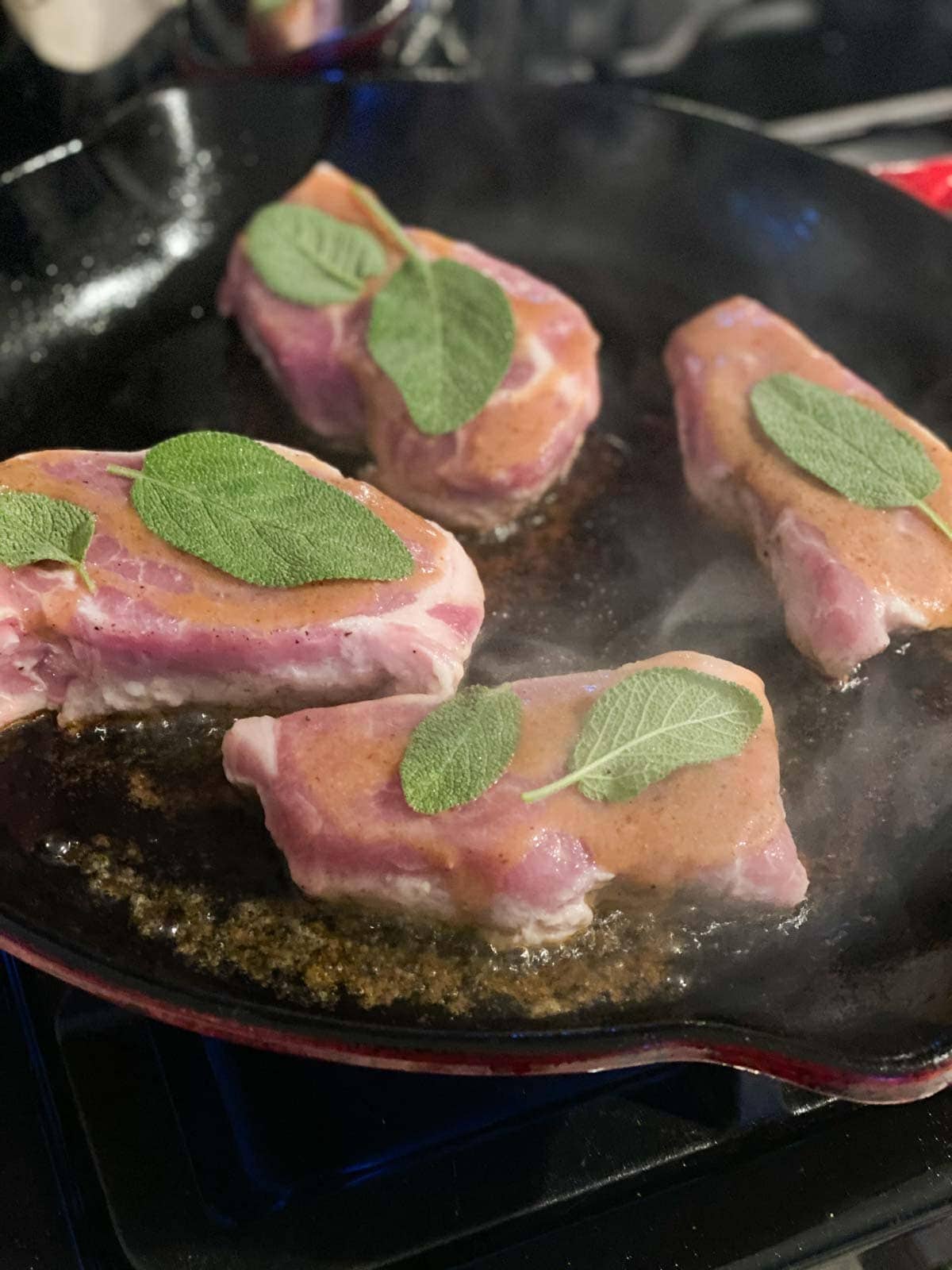 Pork loin chops topped with sage and dijon sauce being seared in a cast iron pan