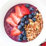 A purple acai bowl with strawberries, blueberries, and granola on top