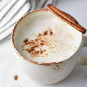 A mug of frothed cinnamon milk with a cinnamon stick and a napkin