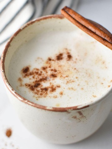 A mug of frothed cinnamon milk with a cinnamon stick and a napkin
