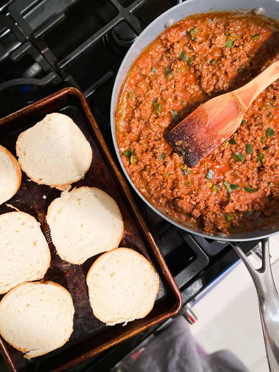 Sloppy joe filling in a pan next to burger buns.