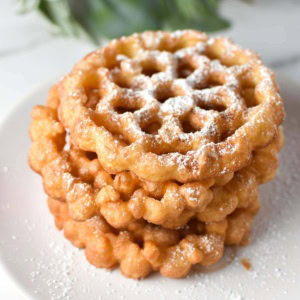 Stacked rosette cookies on a white plate with holly