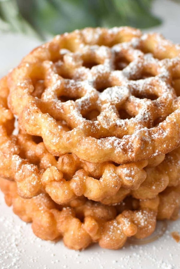 Stacked rosette cookies on a white plate with holly