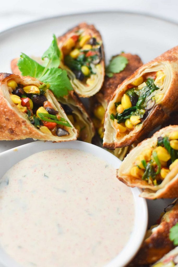 Southwestern egg rolls surrounding a bowl of spicy ranch dipping sauce
