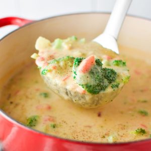 A ladle filled with Boursin broccoli cheese soup coming out of a red pot