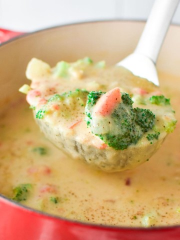 A ladle filled with Boursin broccoli cheese soup coming out of a red pot