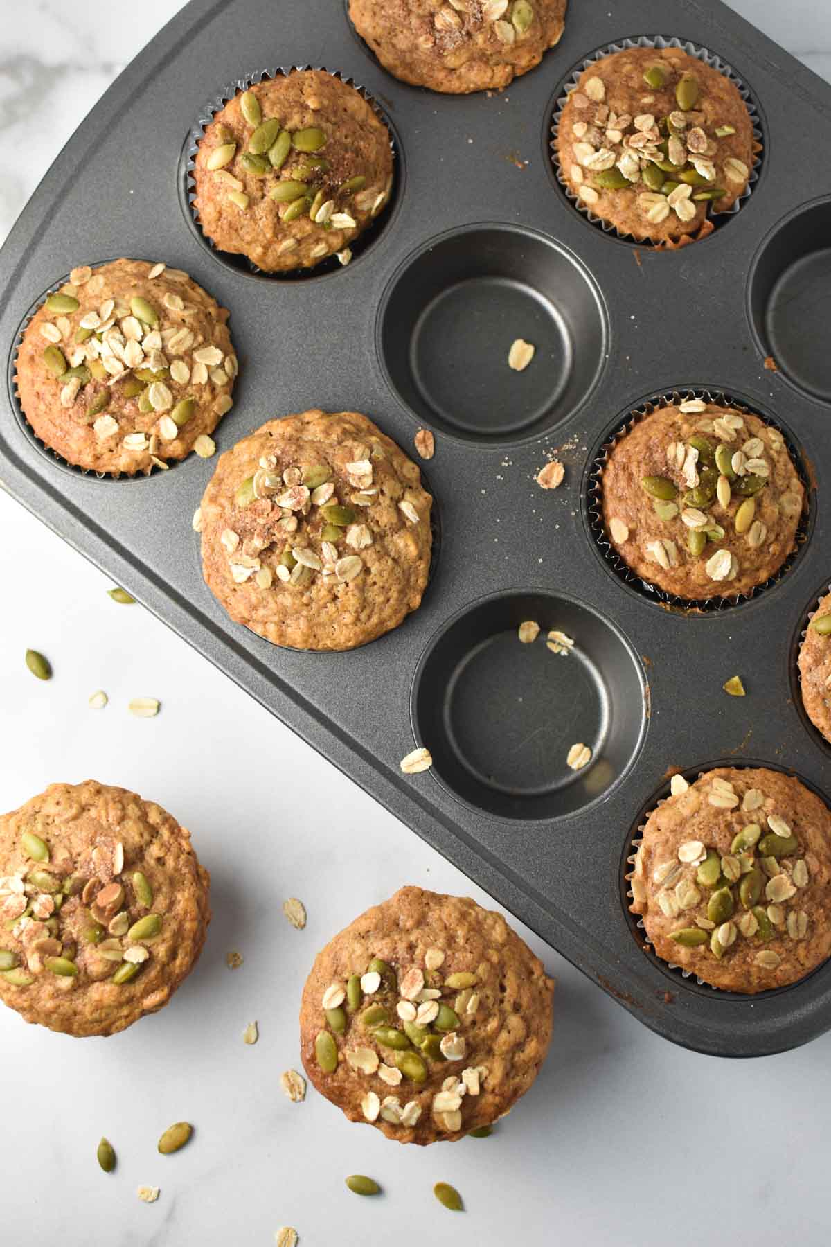 Cinnamon oatmeal muffins in a baking pan topped with seeds and oats.