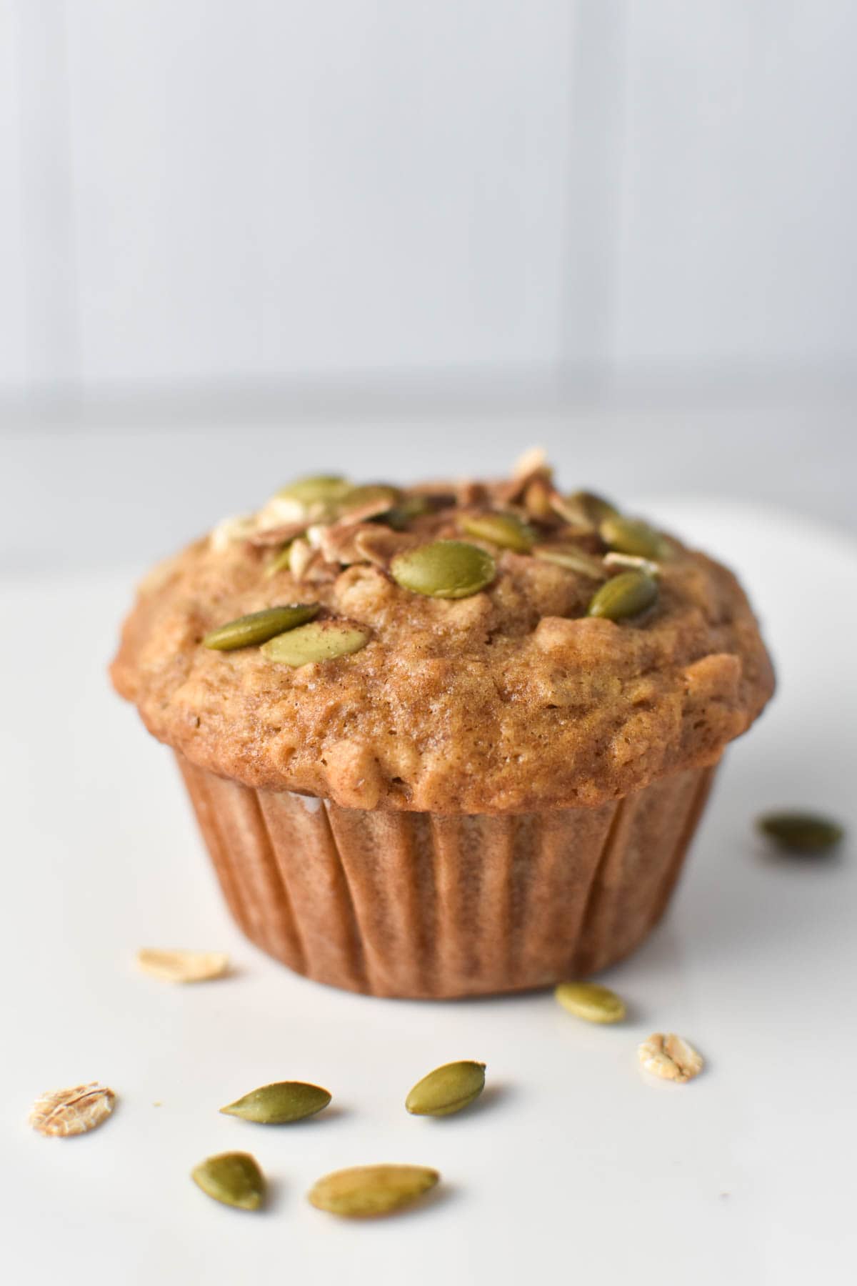 A muffin topped with pepitas and oats on a white plate.