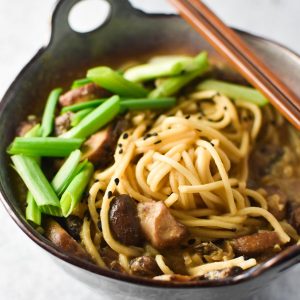 A gray bowl of mushroom ramen topped with green onion and sesame with chopsticks