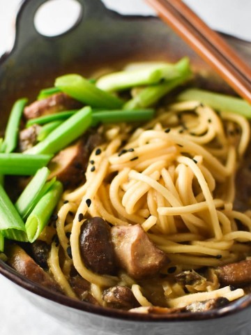 A gray bowl of mushroom ramen topped with green onion and sesame with chopsticks
