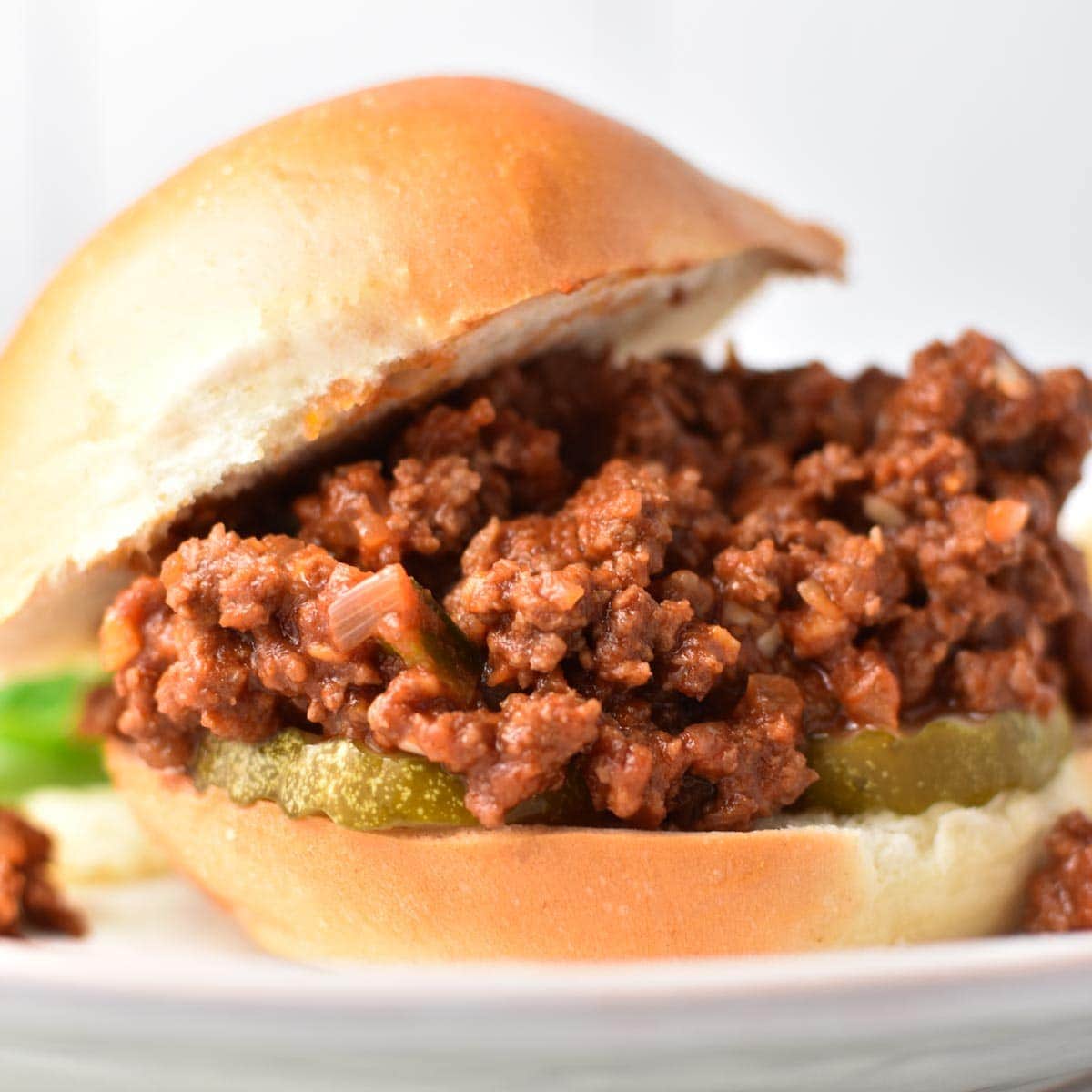 Sloppy joes without ketchup falling out of a bun on a white plate