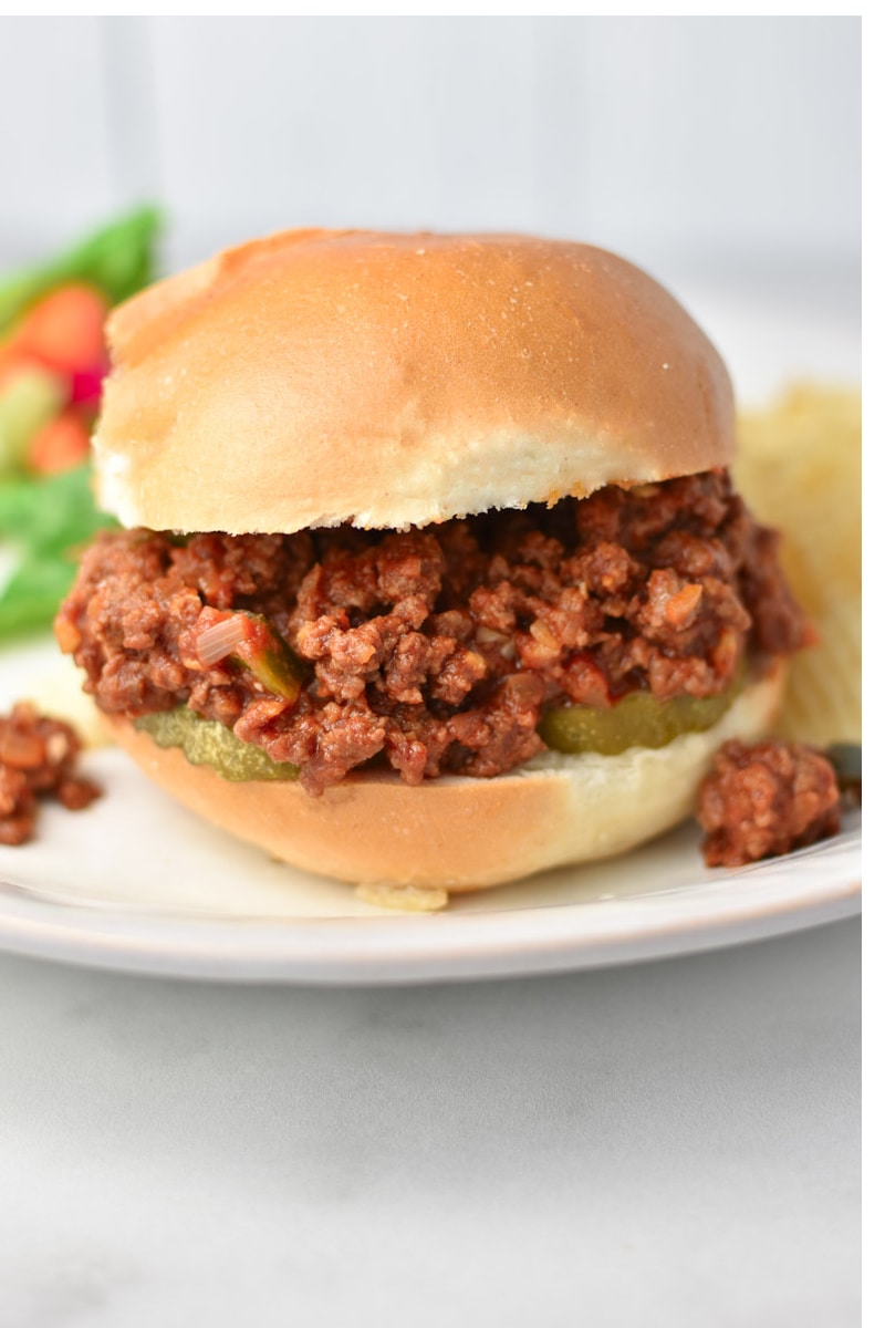 A healthy sloppy joe sandwich with pickles and a salad.