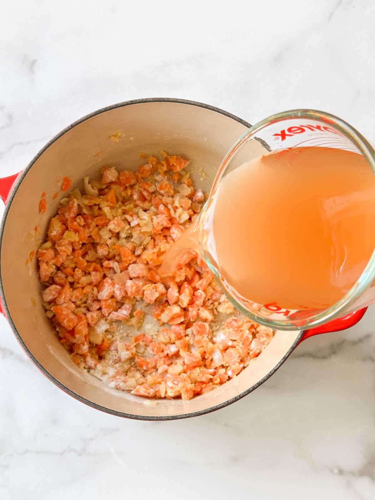Adding broth to the soup pot with flour and vegetables.