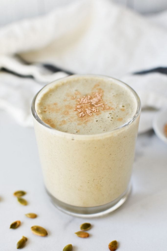 A smoothie topped with lucuma powder next to pumpkin seeds and a napkin
