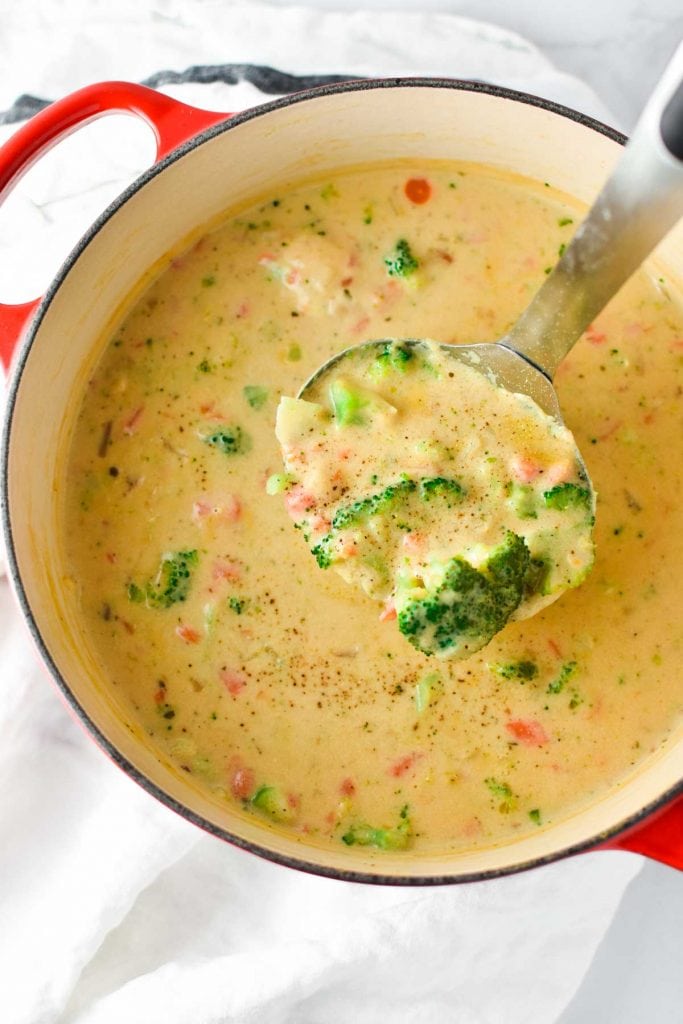 A big ladle full of Boursin broccoli soup coming out of a red pot