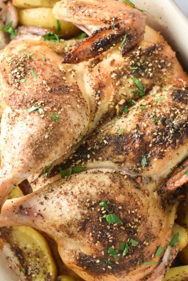 Zaatar roasted chicken on a bed of sumac potatoes and shallots in a roasting dish