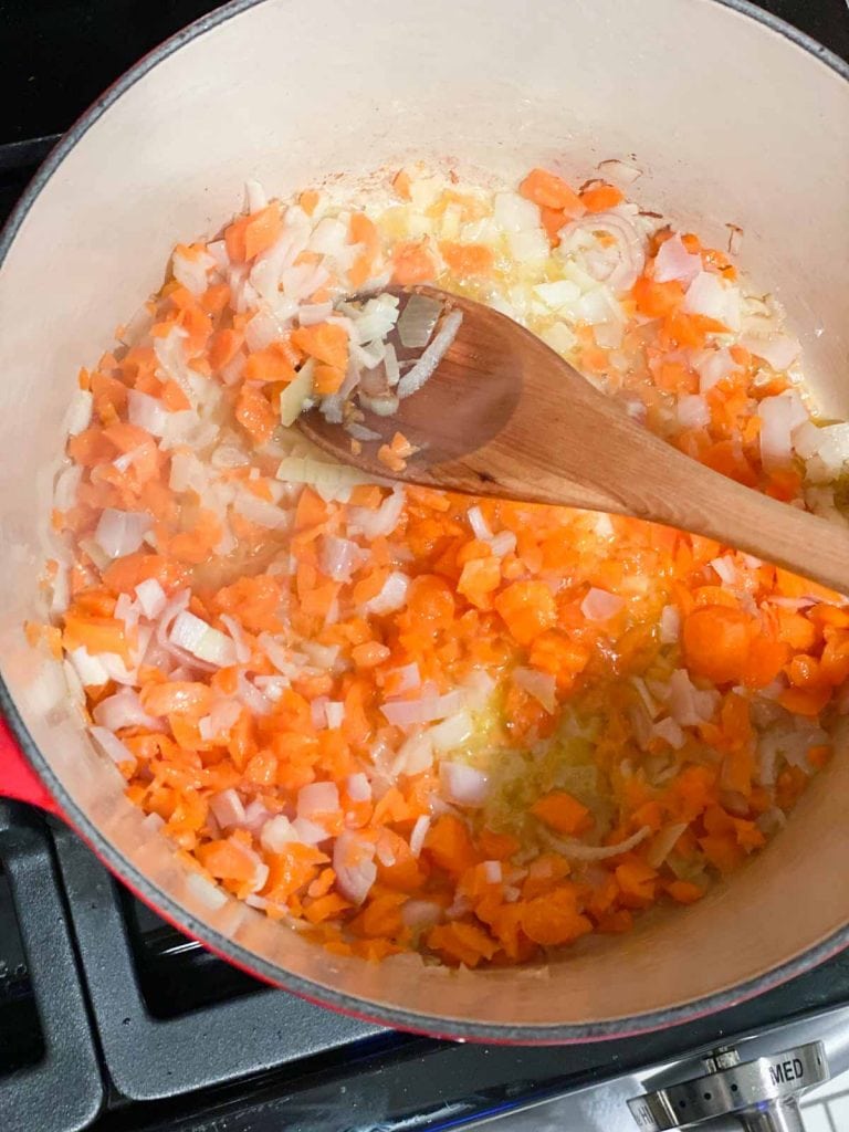A mixture of carrots and shallots being cooked in a dutch oven pot
