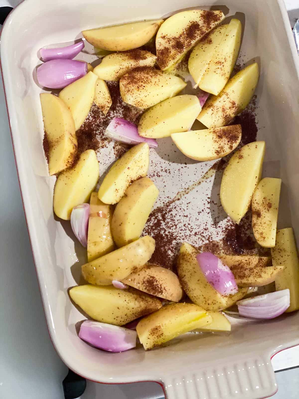 A mixture of wedge potatoes and shallots covered in sumac and olive oil in a roasting pan