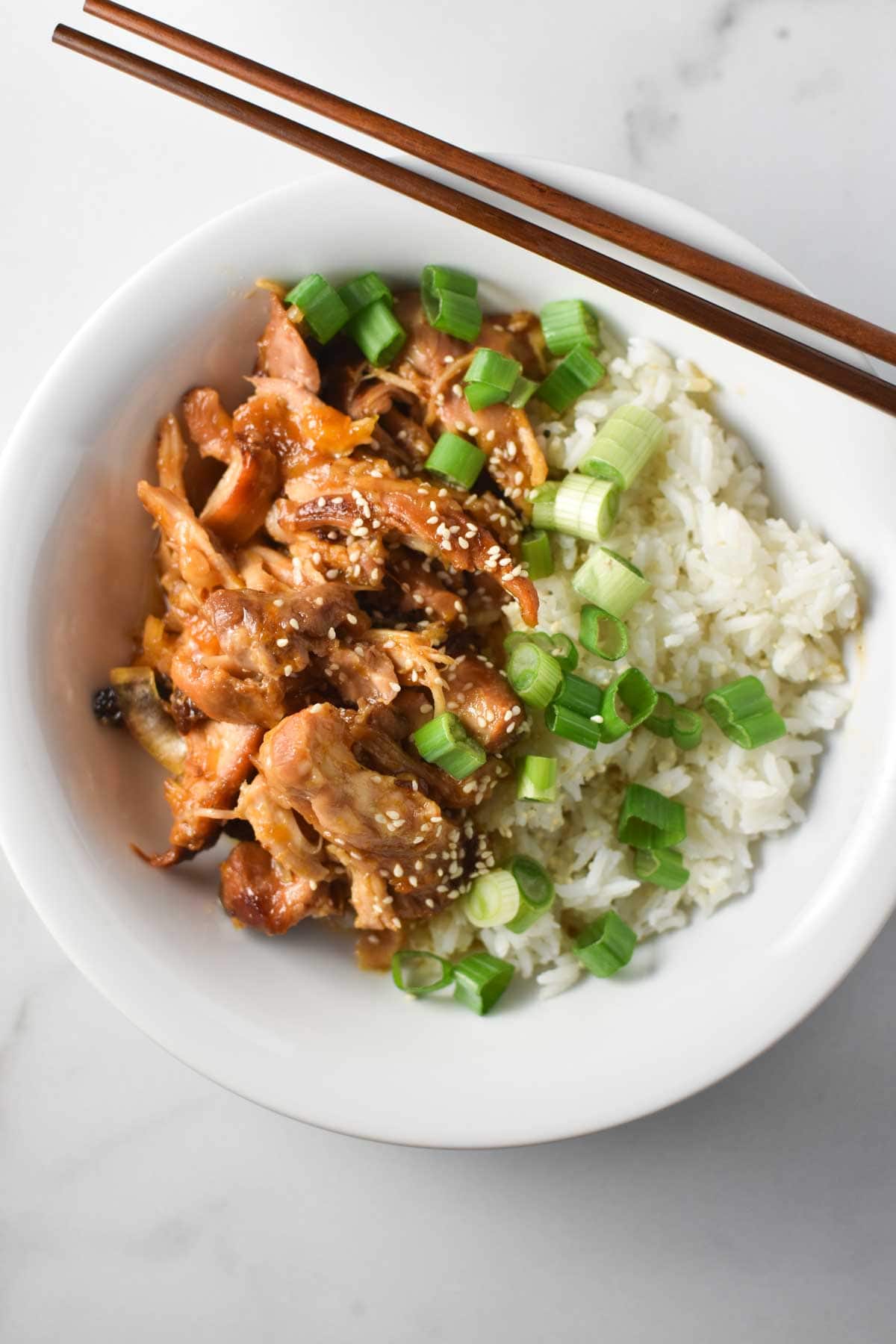 Shredded chicken in apricot sauce next to chopsticks and rice.