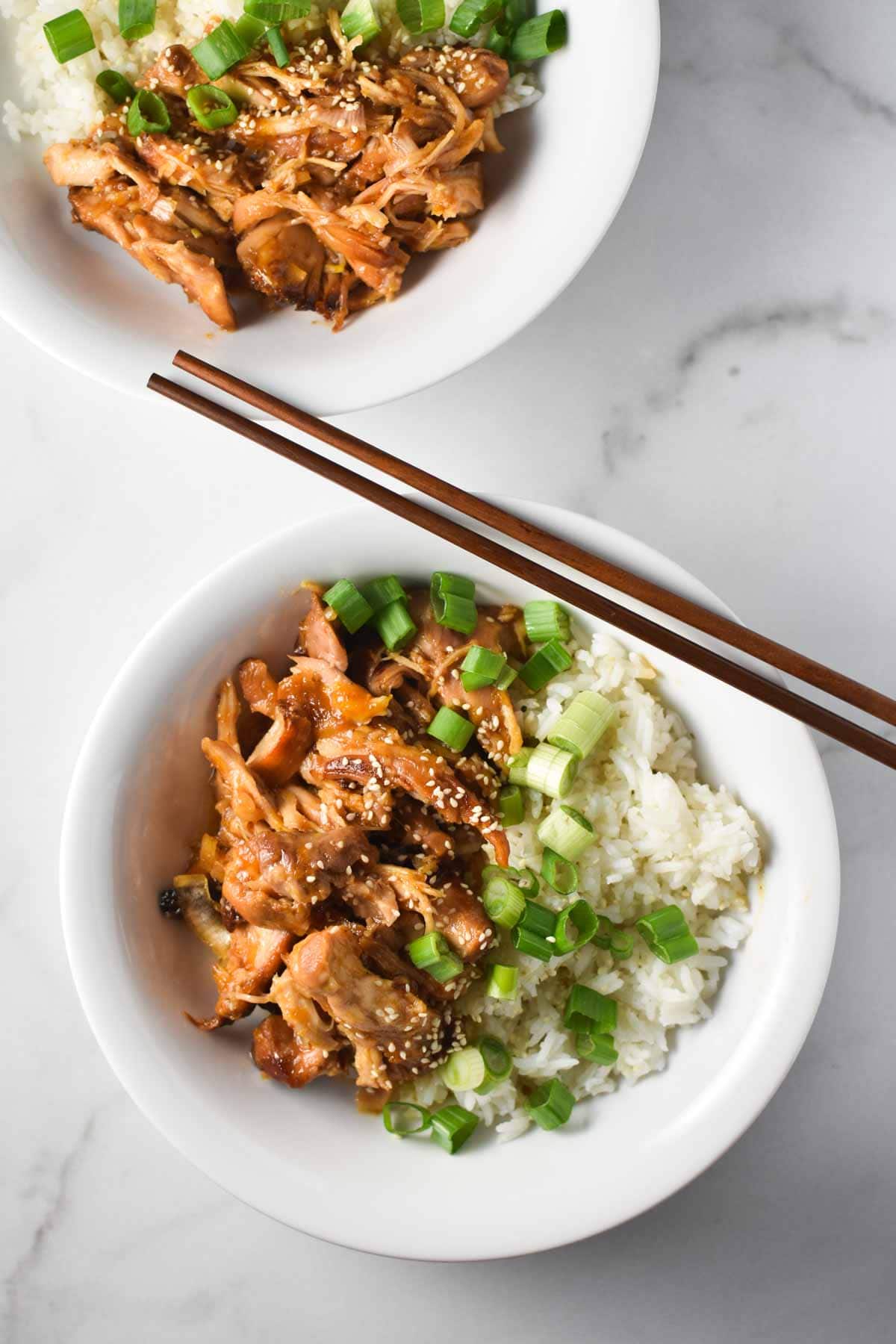 Two bowls of chicken in apricot sauce with rice and chopsticks laying on the side