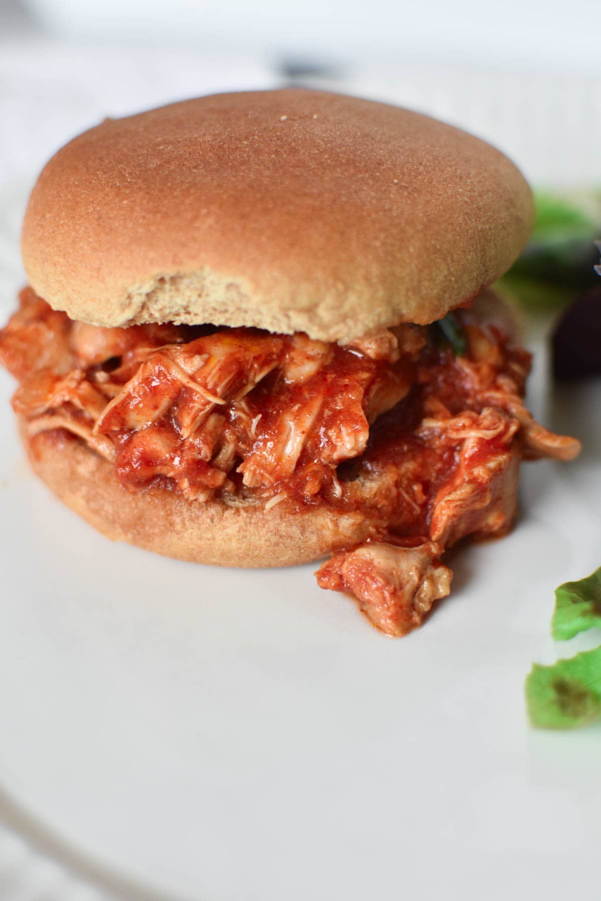 A pulled BBQ chicken thigh sandwich with a salad
