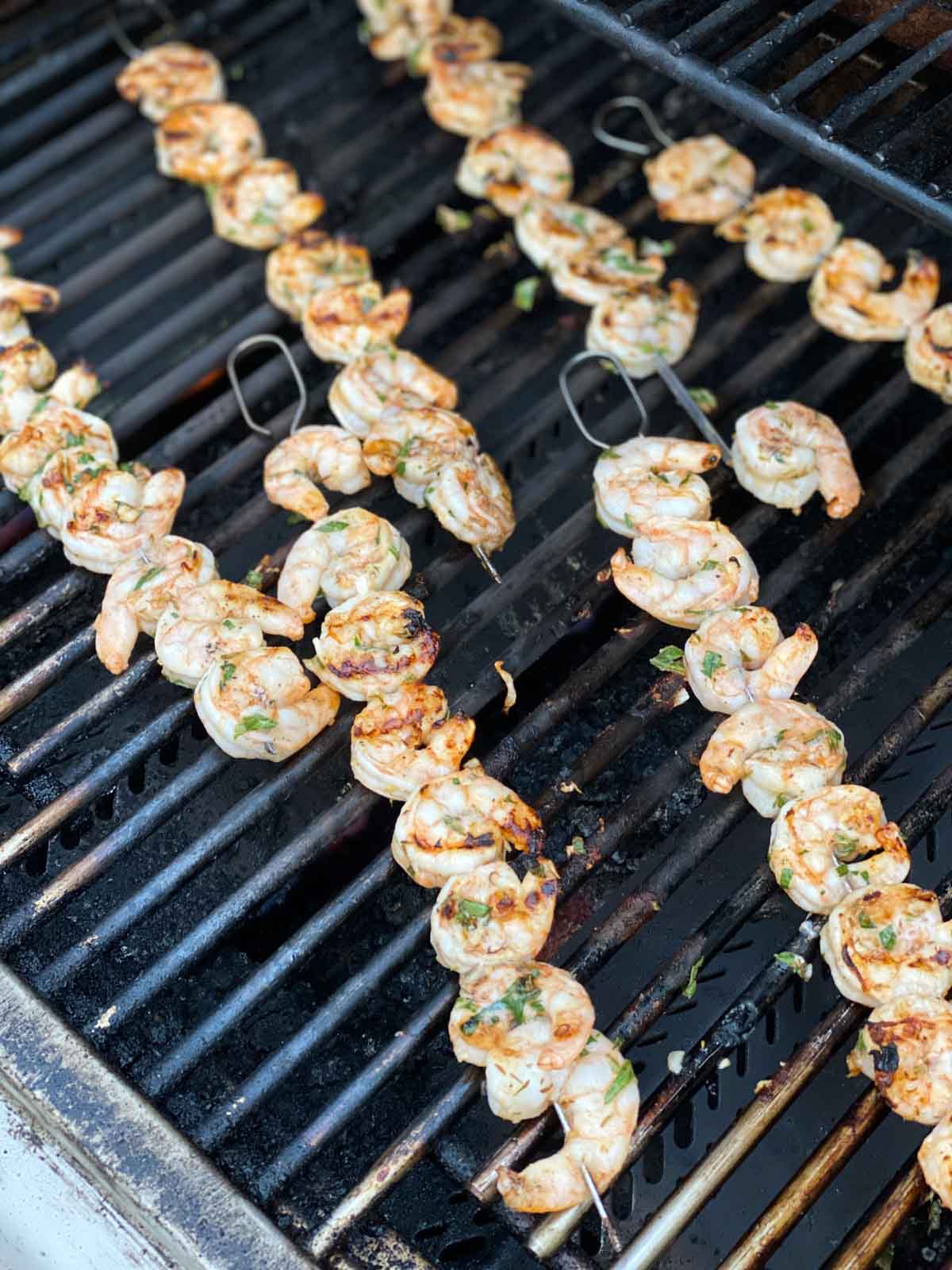 Shrimp on skewers on gas grill grates being flipped to cooked on the other side