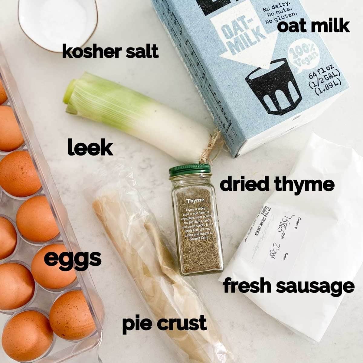 Ingredients for dairy free quiche on a white table including oat milk, eggs, pie crust, and leeks. 