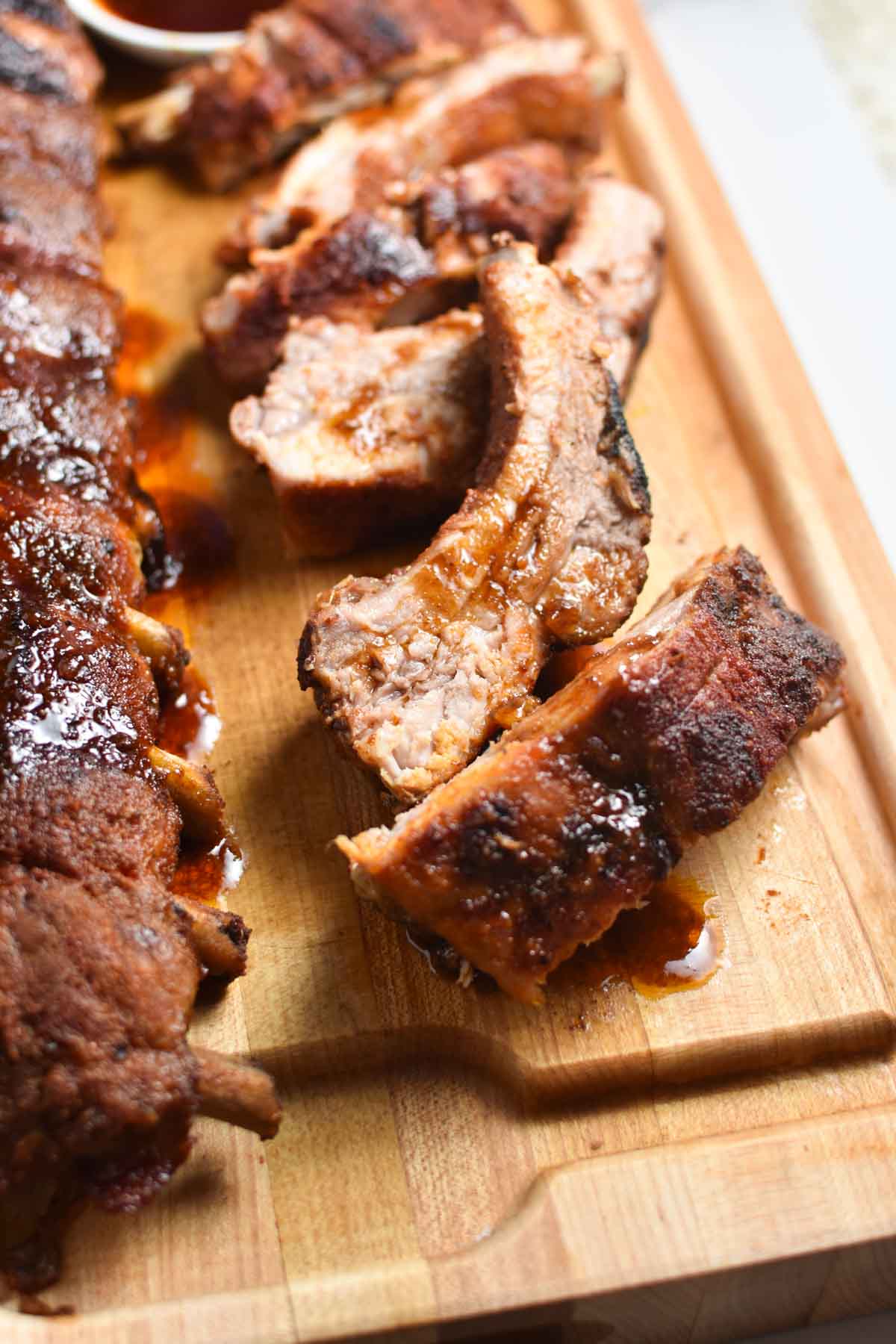 Sliced ribs with BBQ sauce being poured over on a cutting board