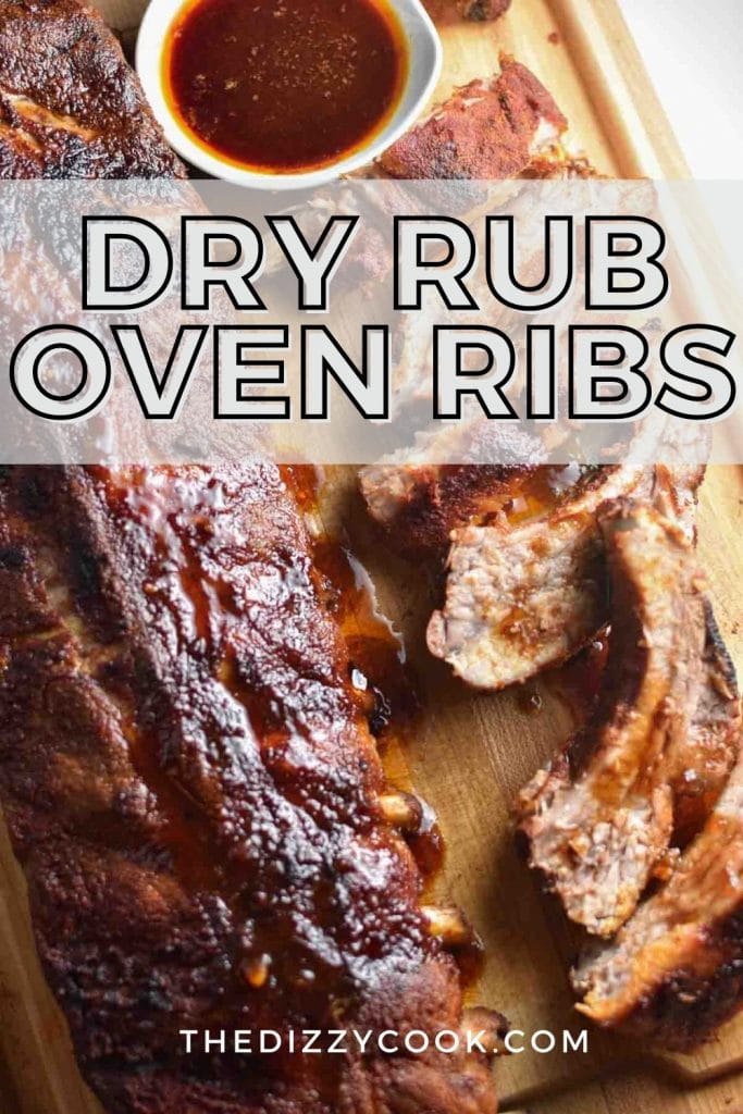 A whole rack of dry rubbed oven ribs next to sliced ribs and bbq sauce on a wooden board