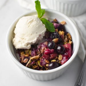 A strawberry blueberry crisp topped with oats and vanilla ice cream with a sprig of mint in a white bowl
