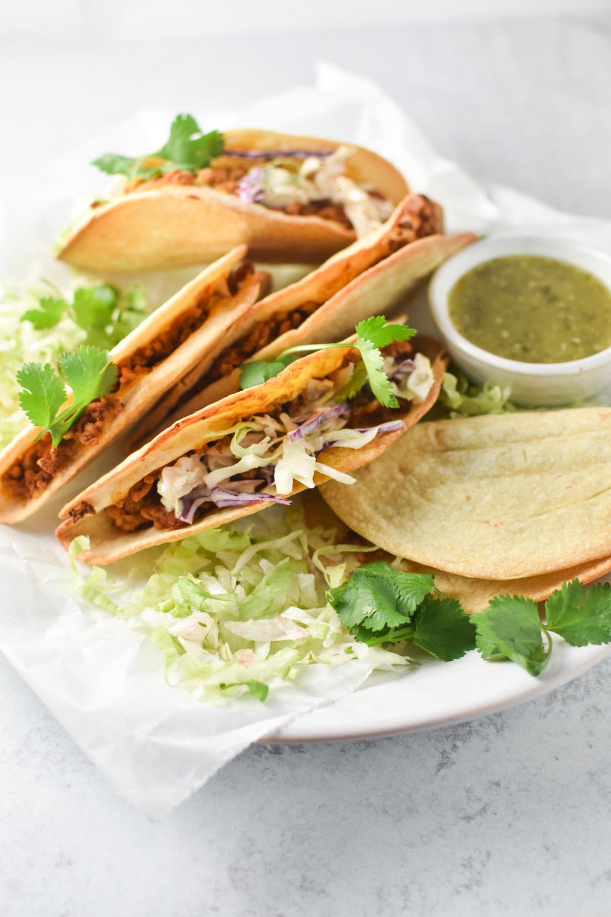 Tacos on a white plate with slaw and lettuce.