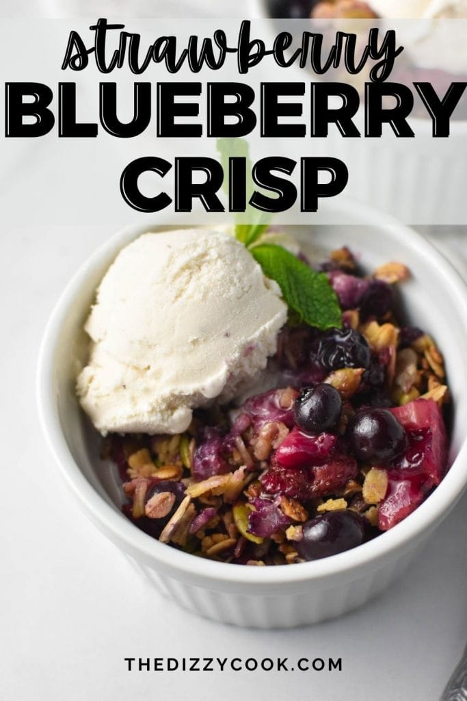 A strawberry blueberry crisp topped with oats and vanilla ice cream with a sprig of mint in a white bowl