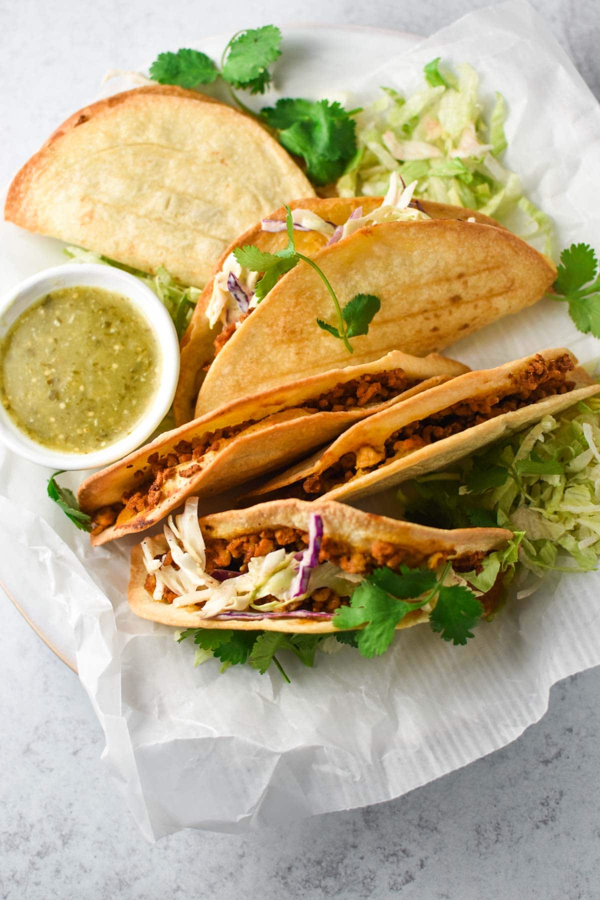 A row of crispy baked tacos on a platter with parchment paper.