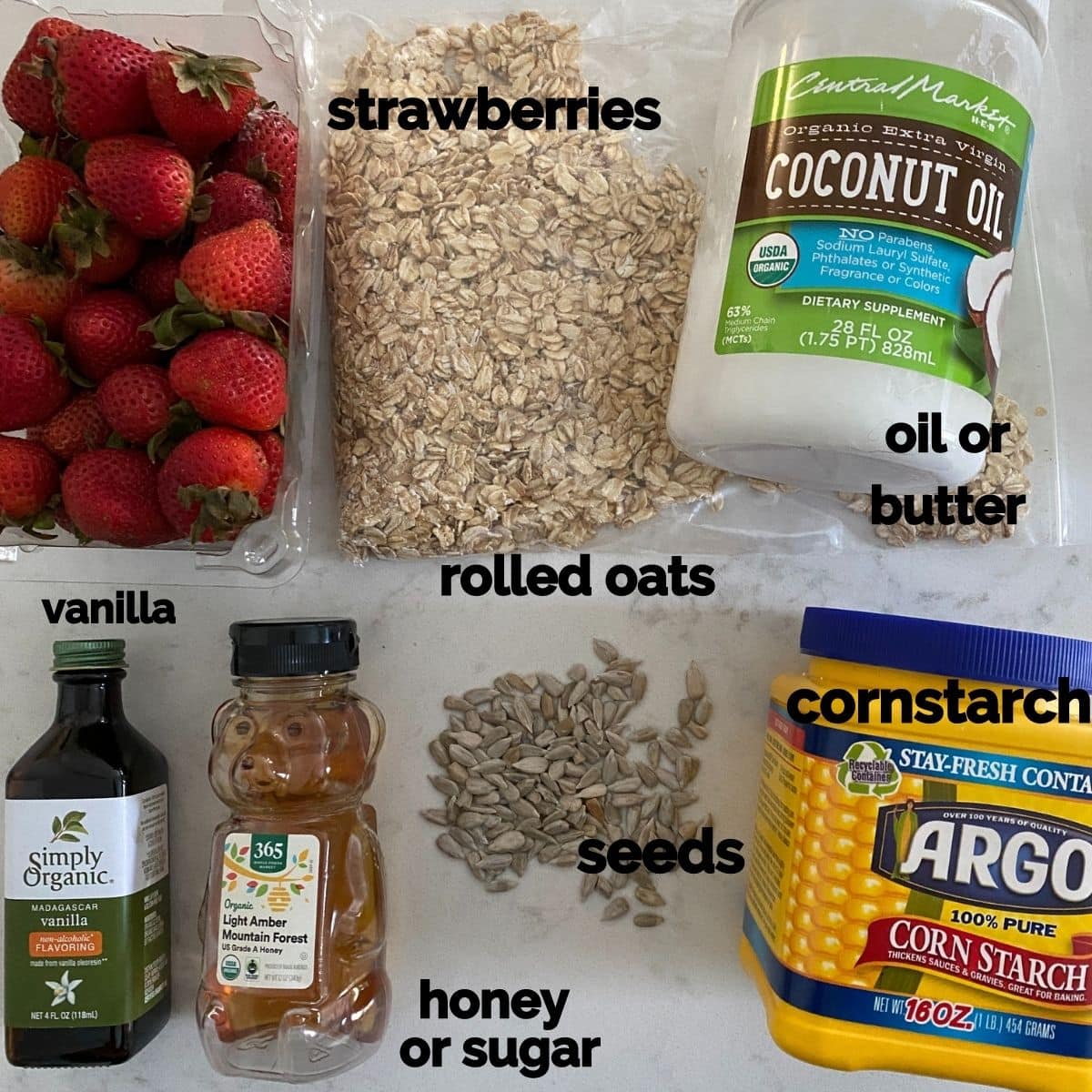 Ingredients for a berry crisp - strawberries, oats, oil, vanilla, sugar, seeds, and cornstarch on a table