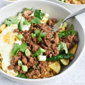 Ground beef, eggs, and green onion in a white bowl with a fork