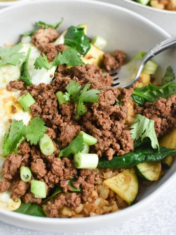 Ground beef, eggs, and green onion in a white bowl with a fork.