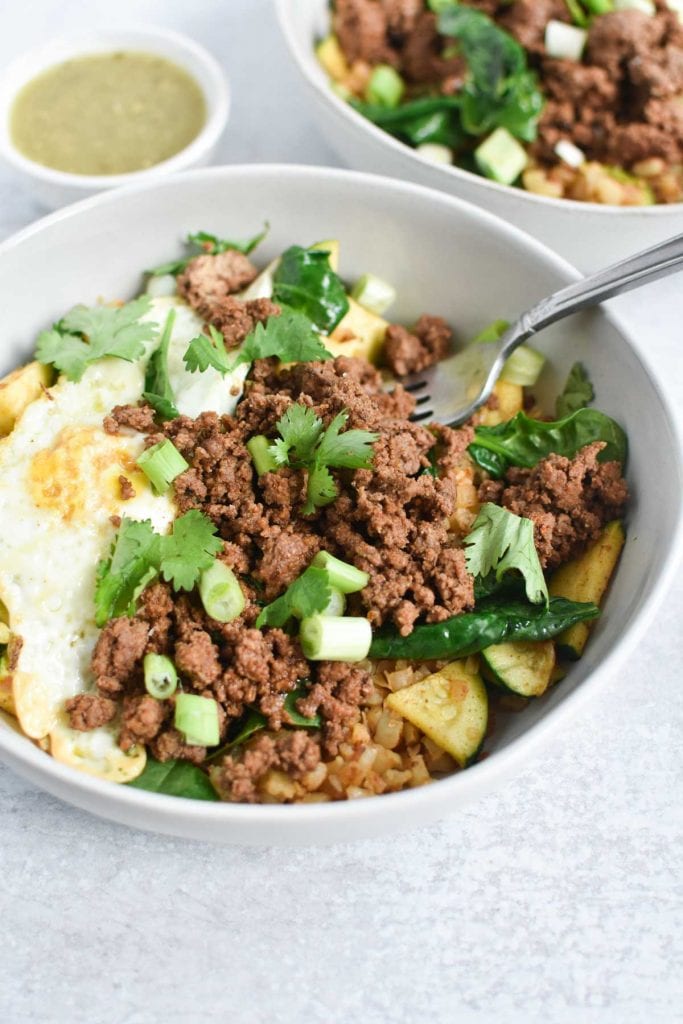 Ground beef, eggs, and green onion in a white bowl with a fork
