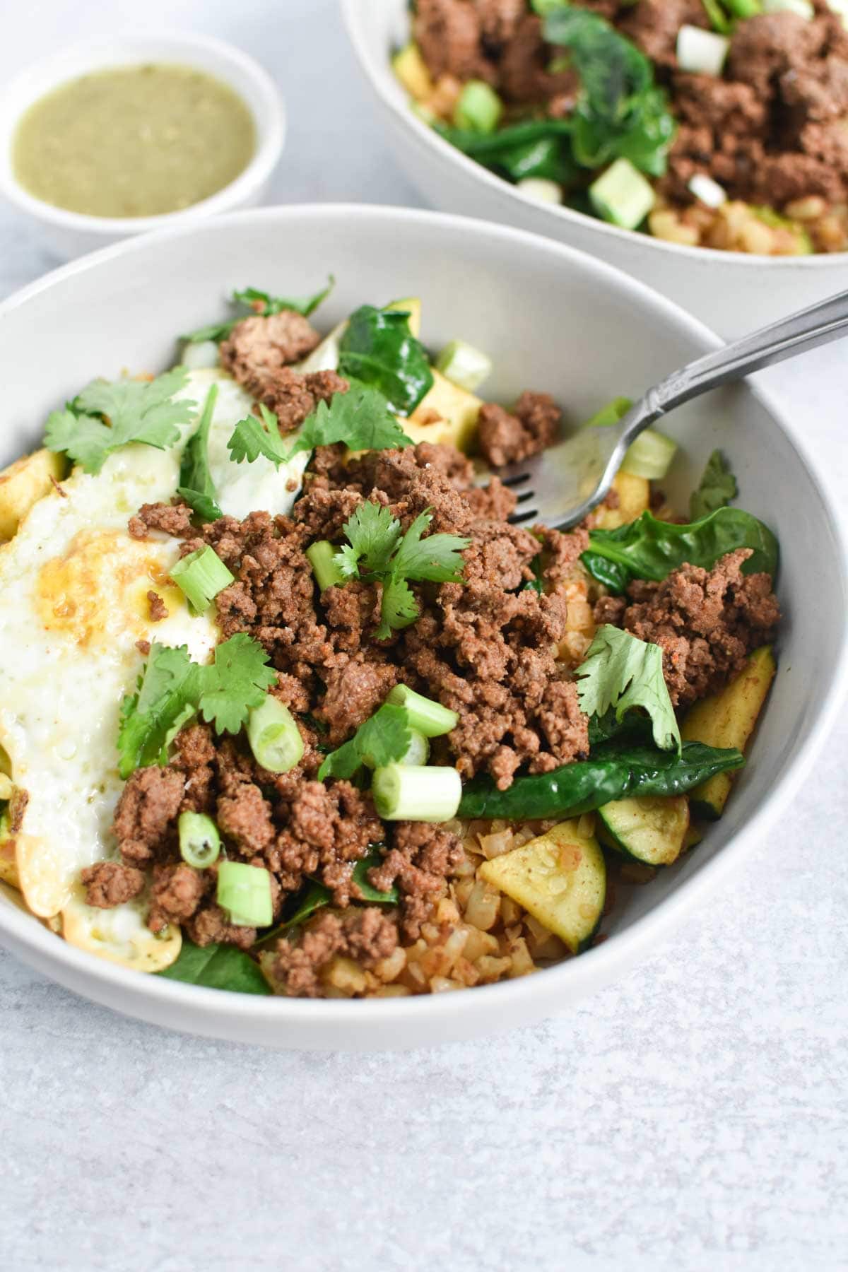 Ground beef, eggs, and green onion in a white bowl with a fork.
