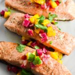 Three filets of grilled salmon topped with a mango salsa on a grey plate