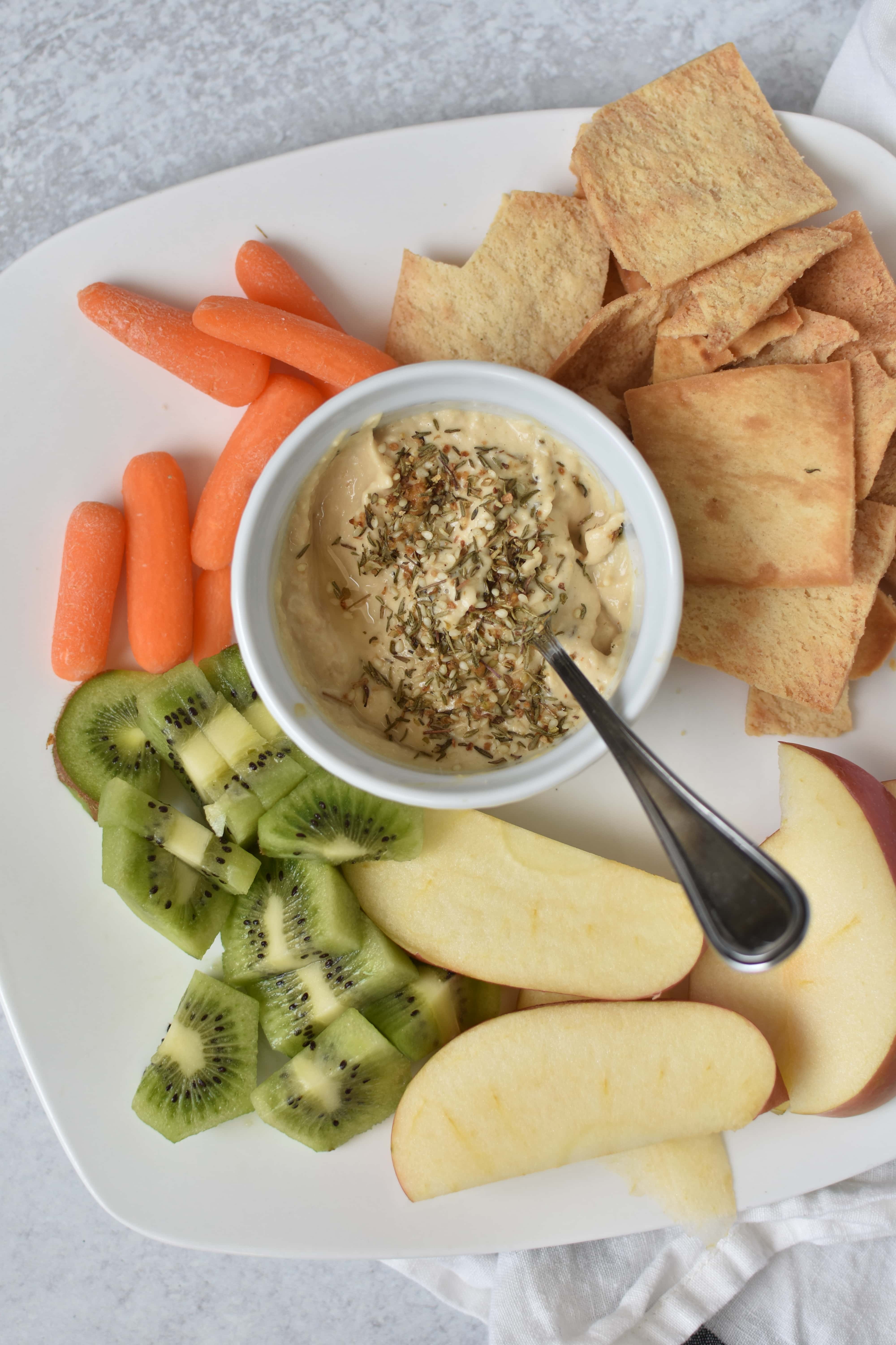 A bowl of hummus with vegetables on a white plate