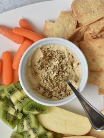 Chips, carrots, apples and hummus on a white plate