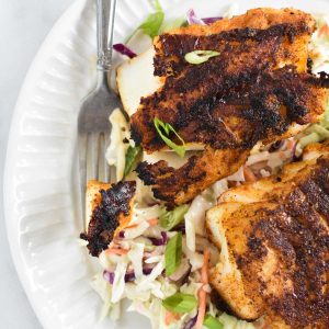 A fork holding a piece of blackened code next to two filets on top of coleslaw